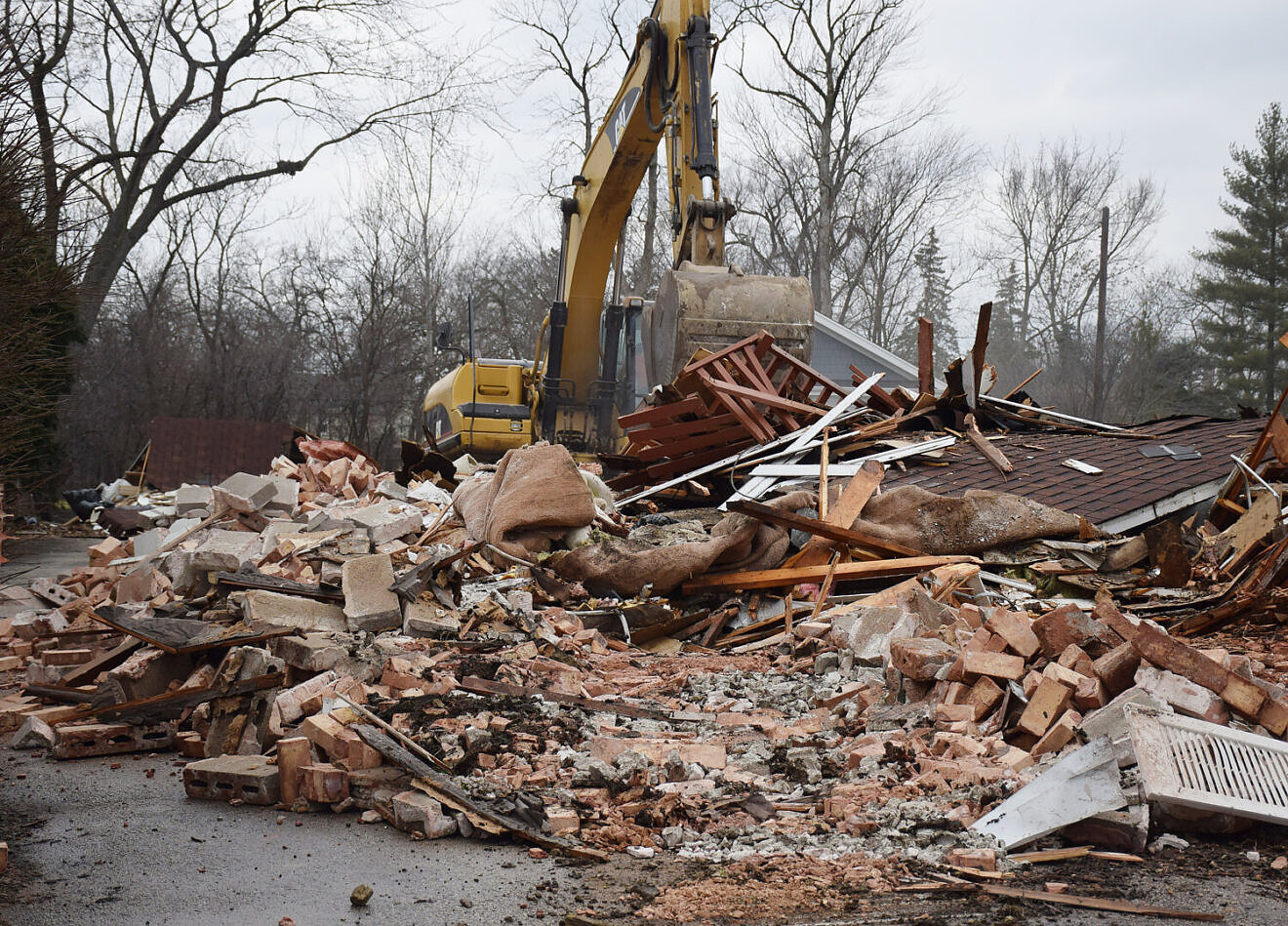 Grävskopa vid rivningsrester av ett hus.
